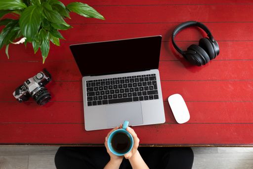 A top view of female hands holding a cup of tea with a laptop, camera, headphones and green plat