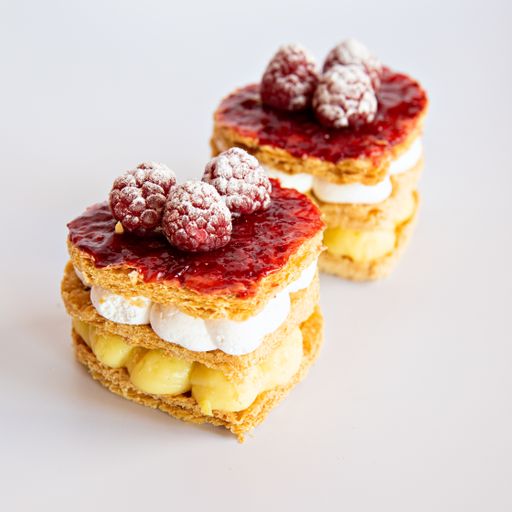 A closeup shot of two cake pieces with raspberry on a white surface background