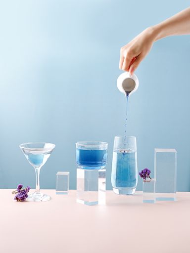 A vertical shot of the hand pouring blue liquid in the different glasses