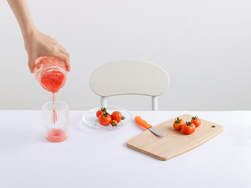 A view of a hand pouring a tomato juice in the glass and vegetable cutting board with a knife near it