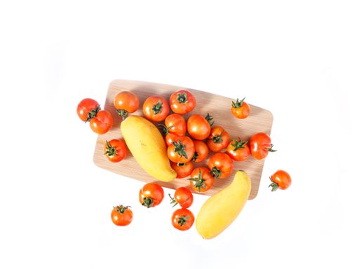 A top view of small red tomatoes with two yellow Zucchinis on a wooden board on a white background