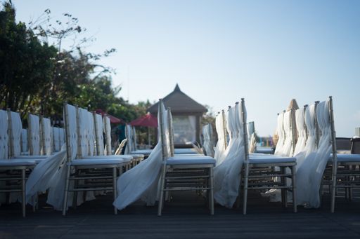 A wide shot of white chairs for a wedding reception during the daytime under the beautiful blue sky