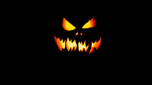 A close-up of a creepy scary lit smiling Halloween pumpkin in the darkness