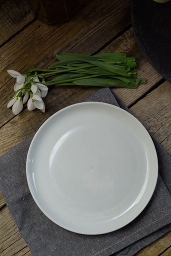 An empty white plate on a wooden table with snowdrop flowers