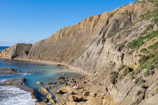 Steep blue clay slopes, with flaking debris forming scree on limestone along the coast of Gozo, in the Maltese Islands, on a beautiful sunny day.
