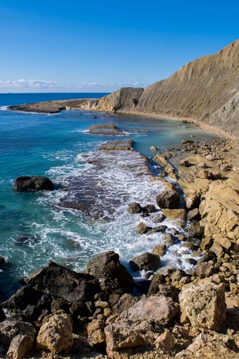 Steep blue clay slopes, with flaking debris forming scree on limestone along the coast of Xatt l-Ahmar, Ghajnsielem, Gozo, Malta, on a sunny day.