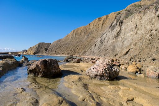 Steep blue clay slopes, with flaking debris forming scree on limestone along the coast of Xatt l-Ahmar, Ghajnsielem, Gozo, Malta, on a sunny day.