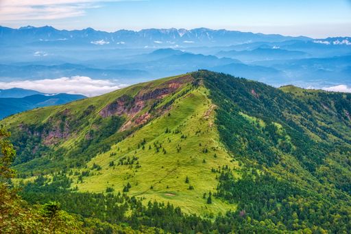 A scenic view of a hill, clouds and mountains