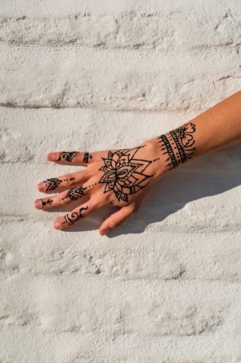 Hand of a woman with henna drawing on brick wall of white color