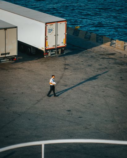 A member of a ship crew walking by cargo trucks with a notebook on a sunny day