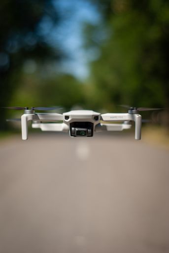 A close-up shot of a white Mavic Mini drone flying outdoors on a blurred background