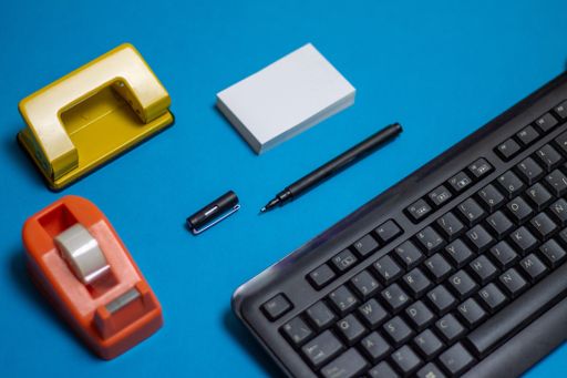 A black computer keyboard next to a pen, papers and other stationery items on a blue background