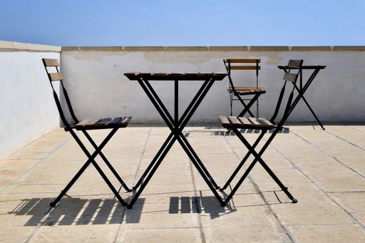 A horizontal shot of a table and two chairs on a balcony during day with chairs in the background