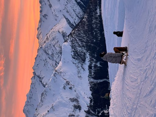 A vertical shot of people skiing against a mountain range covered with snow at sunset