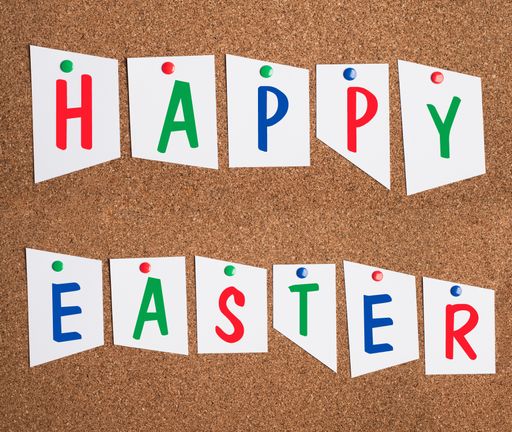 Happy Easter is standing on pinned paper on a cork wall, holiday greetings in spring, colorful festive card