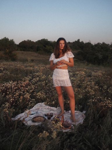 A vertical shot of a woman in white clothing standing on a blanket in a field