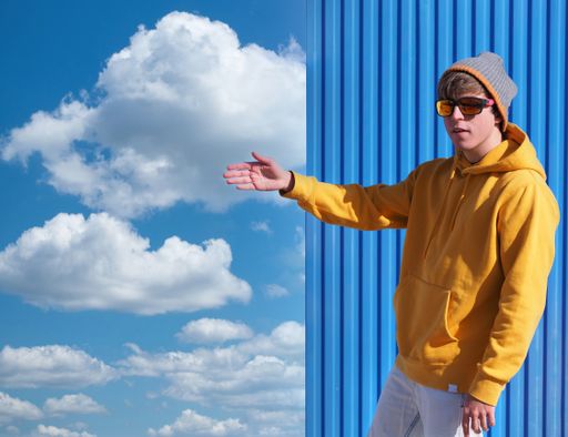 A cheerful young man in a yellow sweatshirt and wool hat pointing to the blue sky with clouds