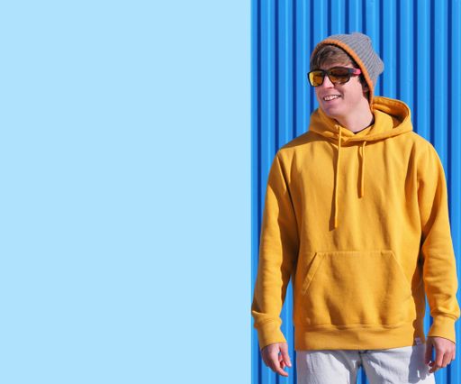 A cheerful young man in a yellow sweatshirt and wool hat pointing to the blue sky with clouds