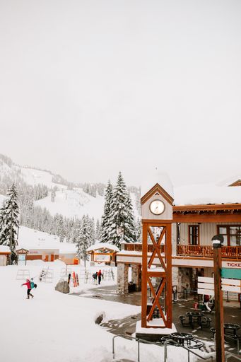 A vertical shot of people standing in the field covered with snow near white and brown wooden house