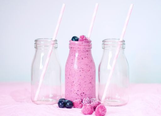 A closeup shot of bottles, one bottle filled with berry smoothie with berries in front of it
