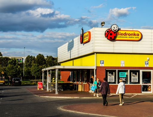People walking to a Biedronka supermarket with parking lot.