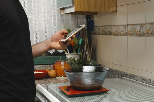 A man holding a smartphone while scaling the dough on a weighing scale