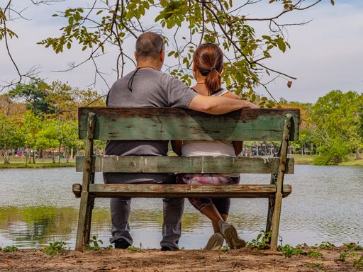 A couple sitting on a slanted park bench in a beautiful scenic park with a lake in front of them in Bangkok, Thailand.