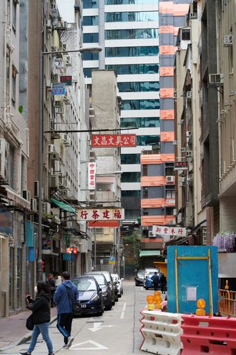 A vertical shot of a street with residential highrise buildings, cars and walking people in Hong Kong