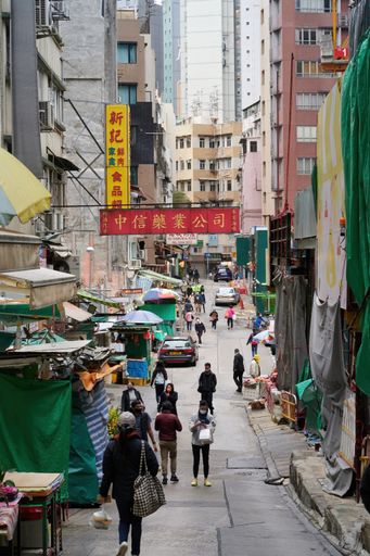 A vertical shot of a street with markets and stalls full of people and residential buildings in Hong Kong