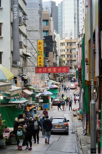 A vertical shot of a street with markets and stalls full of people and residential buildings in Hong Kong