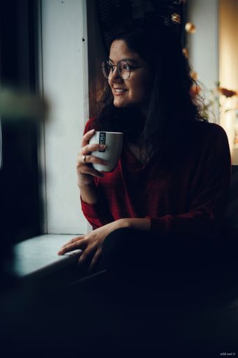 A vertical shot of young indian woman sitting around window and drinking tea