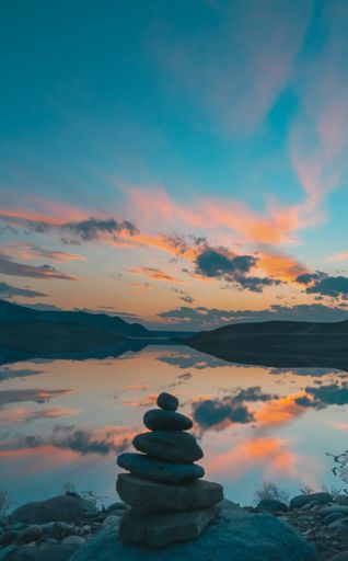 A vertical shot of stone stack on the background of a lake reflecting the orange-blue cloudy sky