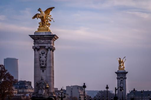 A stunning view of two golden sculptures on top of pillars on a bridge called "Pont Alexandre III" in Paris, France