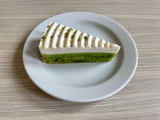 A piece of delicious pistachio cake with whipped cream and topped with chopped pistachios.
