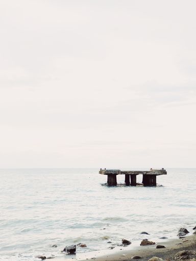 A vertical shot of sea with a small pier on a bright sunny day