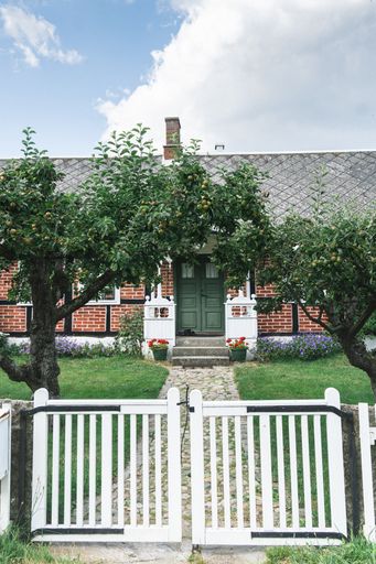 A closeup of a white garden gate with a path to an old brick house in Sweden