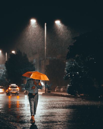 A vertical shot of a man with a yellow umbrella walking home on a rainy night after a hard day's work