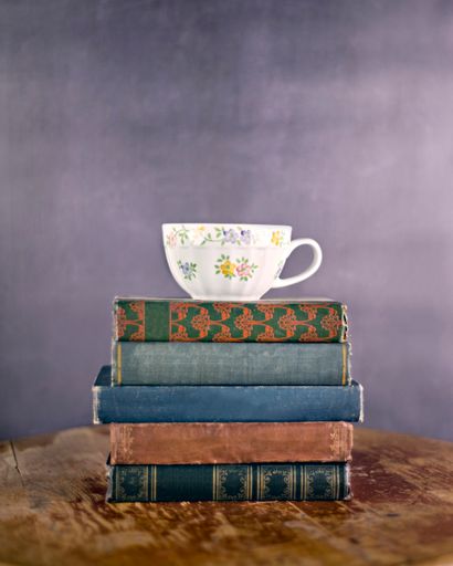 A vertical shot of a teacup on a stack of vintage books