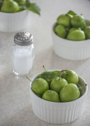 A vertical high angle shot of small green apples in white bowls and salt on a table