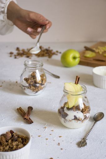 A vertical shot of a female preparing healthy breakfast in glass bowls with apple slices