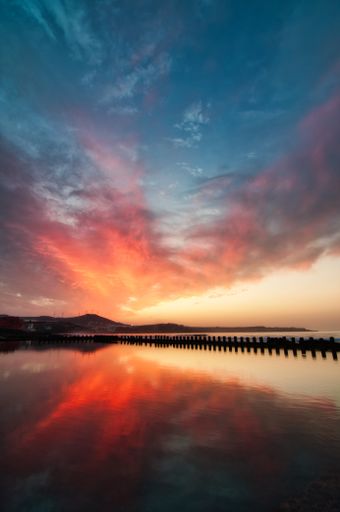 A vertical breathtaking view of a calm sea under a cloudy sky at sunset