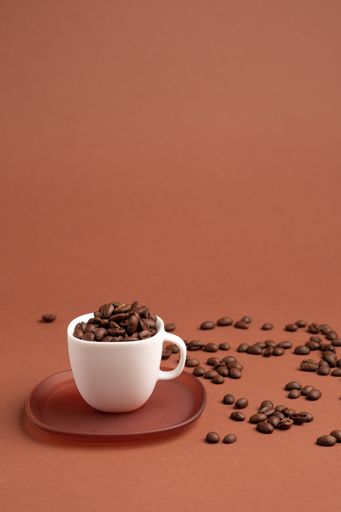 A vertical shot of a white cup filled with coffee beans on the pink background