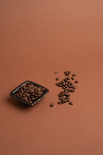 A vertical shot of a black bowl filled with coffee beans on the pink background