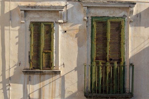 The facade of an old ancient buildings with green aged window and balcony under a sunlight