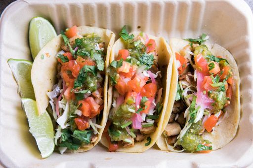 An overhead shot of street tacos with limes in take away box