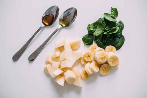 A top view of chopped bananas, apples, and spinach for a healthy smoothie isolated on a white background