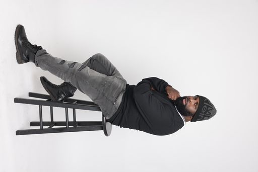 A vertical shot of a trendy Afro-American male wearing a Calvin Klein hat, sitting on a chair in a studio