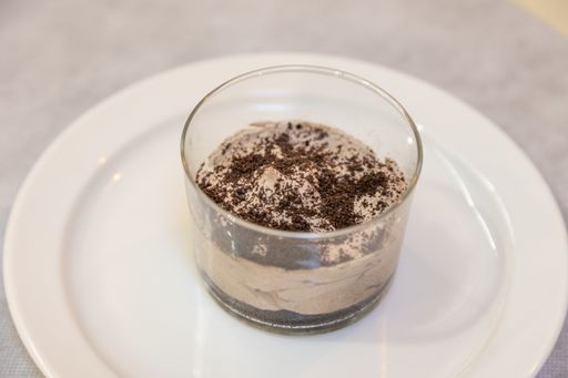 A close-up shot of a pudding with cocoa powder on top, in a glass bowl, on a white plate