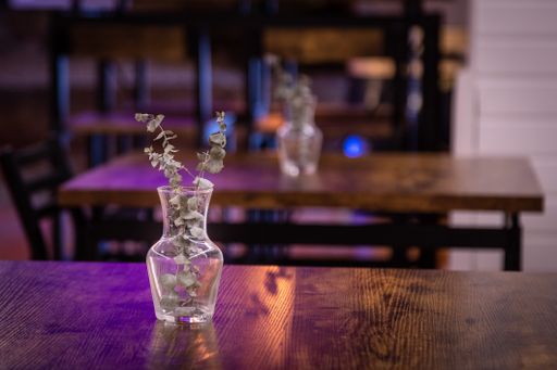 A shallow focus shot of a vase with a decorative plant in it, on a wooden table in a restaurant