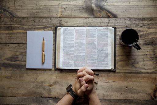 An overhead shot of male's hand near an open book and coffee mug on a wooden surface